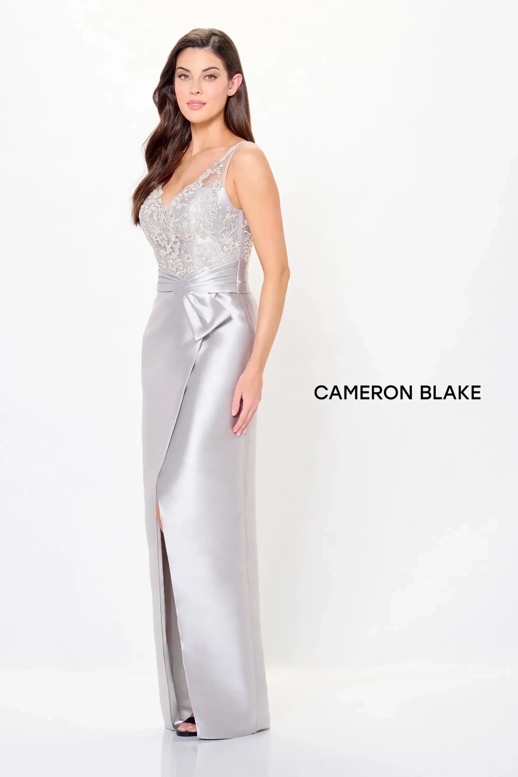 A woman is wearing a silver evening gown with intricate beadwork on the neckline and a side slit. The gown is form-fitting and elegant.