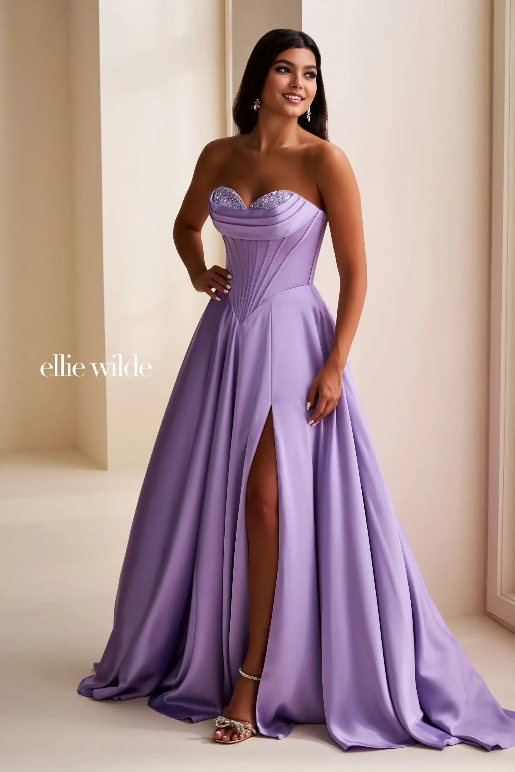 A woman wearing a lavender strapless gown with a split, standing in an elegant setting.