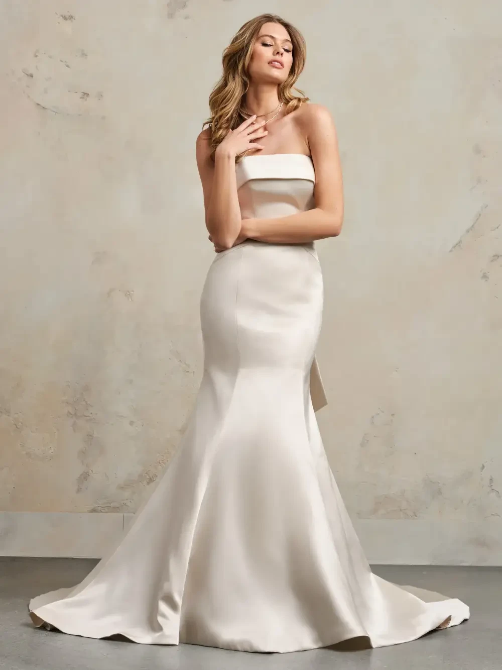 A woman wearing a strapless, flowing wedding gown poses gracefully against a neutral background.