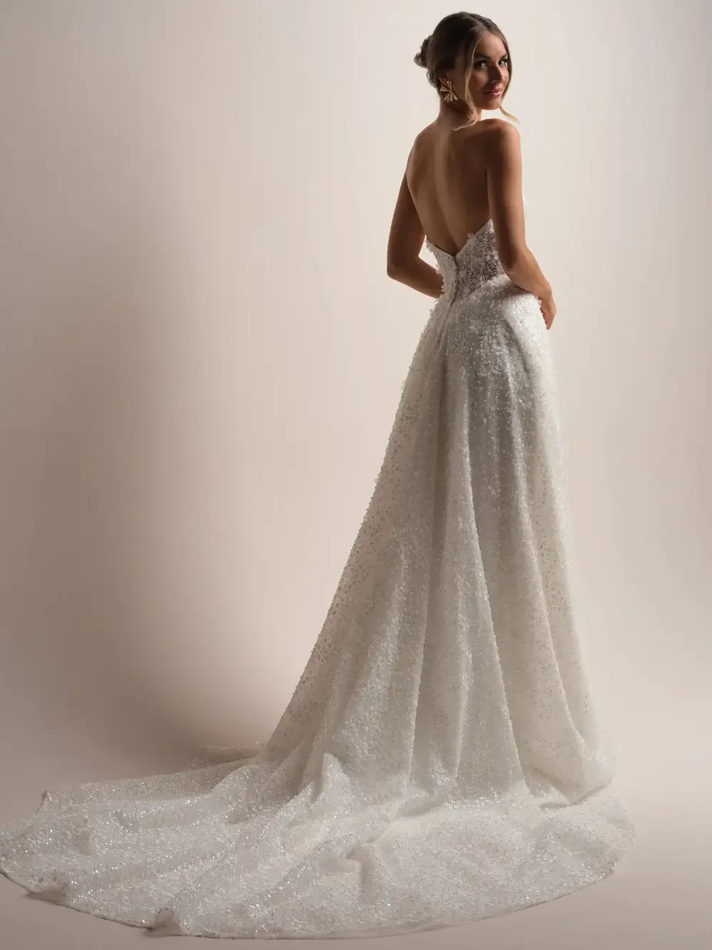 A woman wearing a sparkling white gown with an open back, posing elegantly.